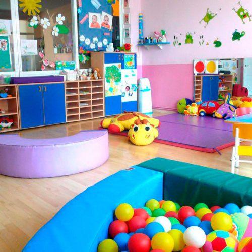 Aula con piscina de bolas en primer plano y zonas de juegos con colchonetas de colores